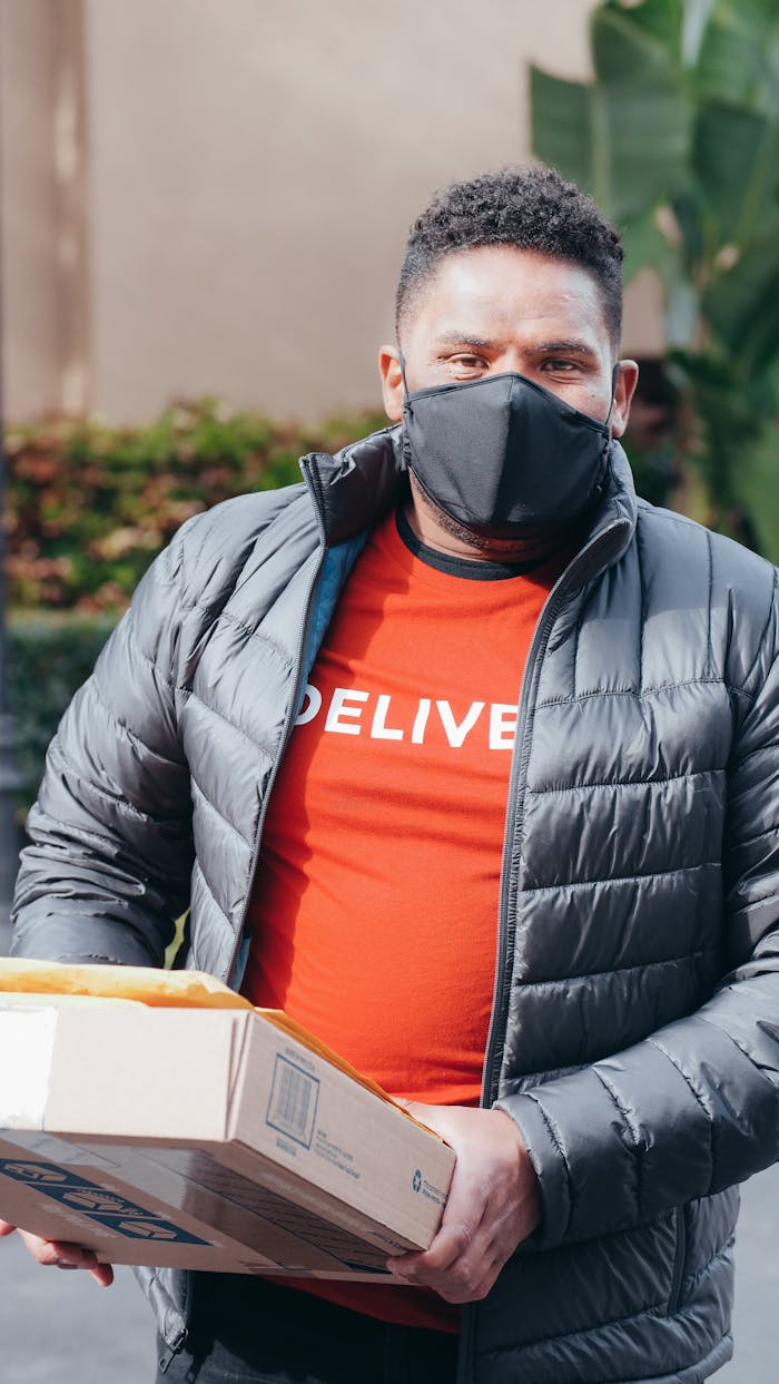 Courier wearing face mask delivering package during daytime. Safety measures in delivery services.