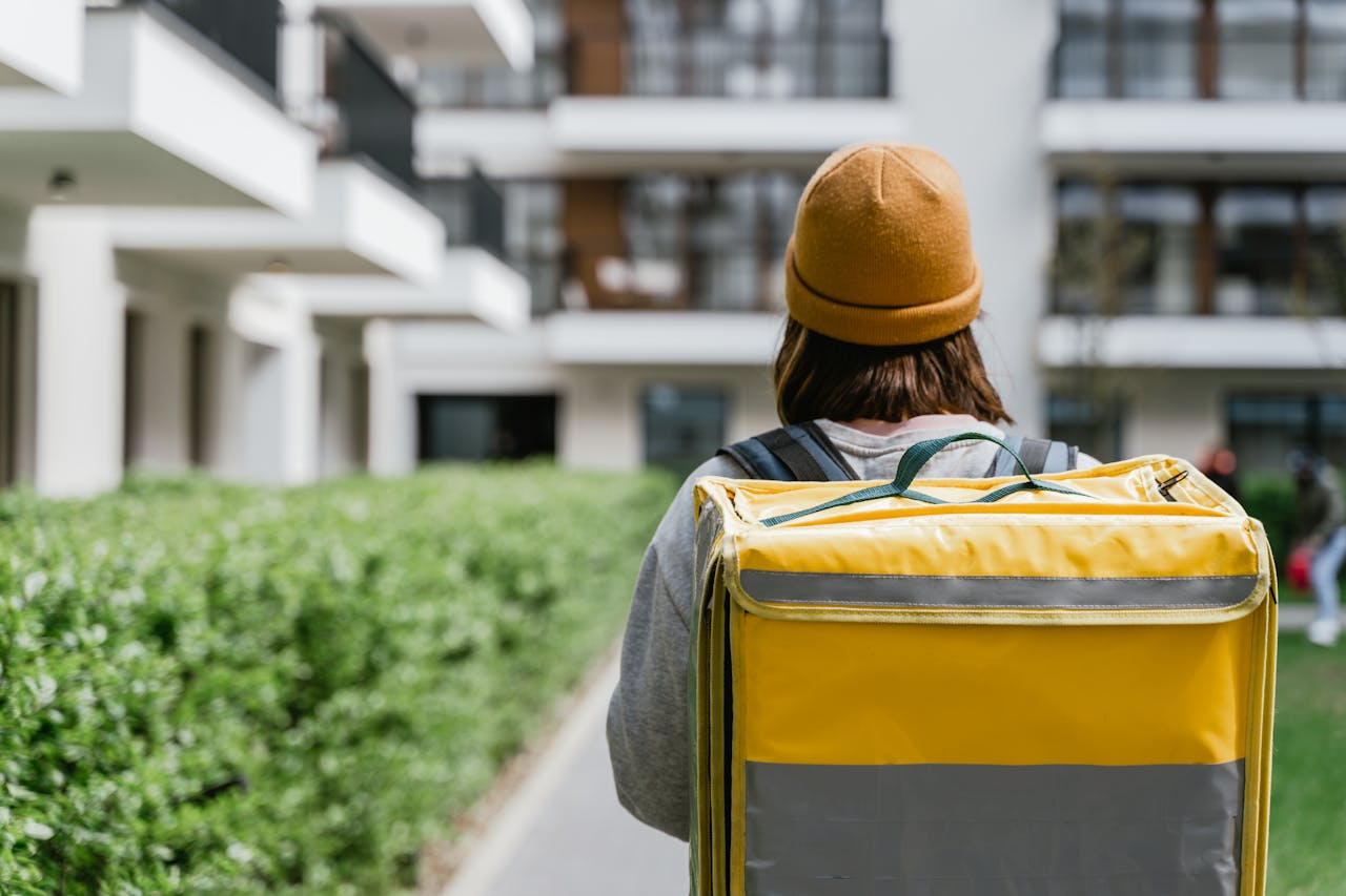Courier carrying yellow thermal bag delivering food in modern urban setting.